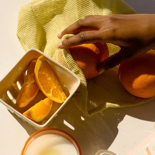 Oranges in a yellow market bag with slides pieces in a bowl.